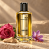 Mancera Aoud Sandroses beside a pink rose, purple saffron crocus, and sandalwood on pale limestone in warm sunlight.