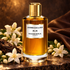 Mancera Jasmin Exclusif on warm dark stone with white jasmine, oud wood and brown leather in amber light.