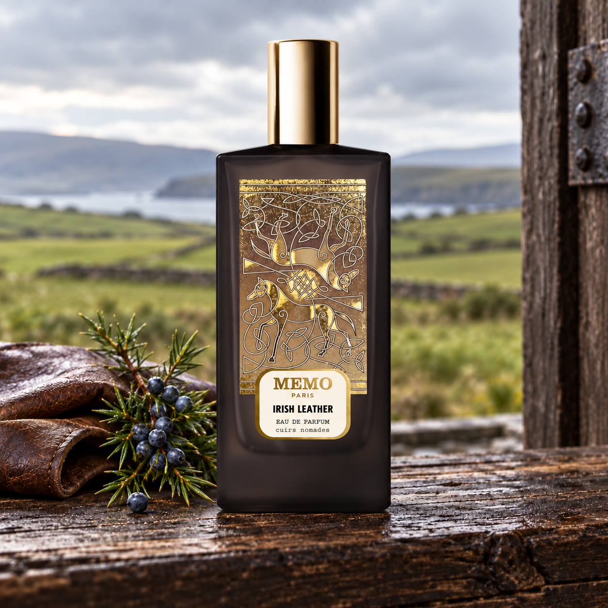 Memo Paris Irish Leather on weathered stable wood with leather and juniper berries, overlooking a green Irish landscape under gray skies.