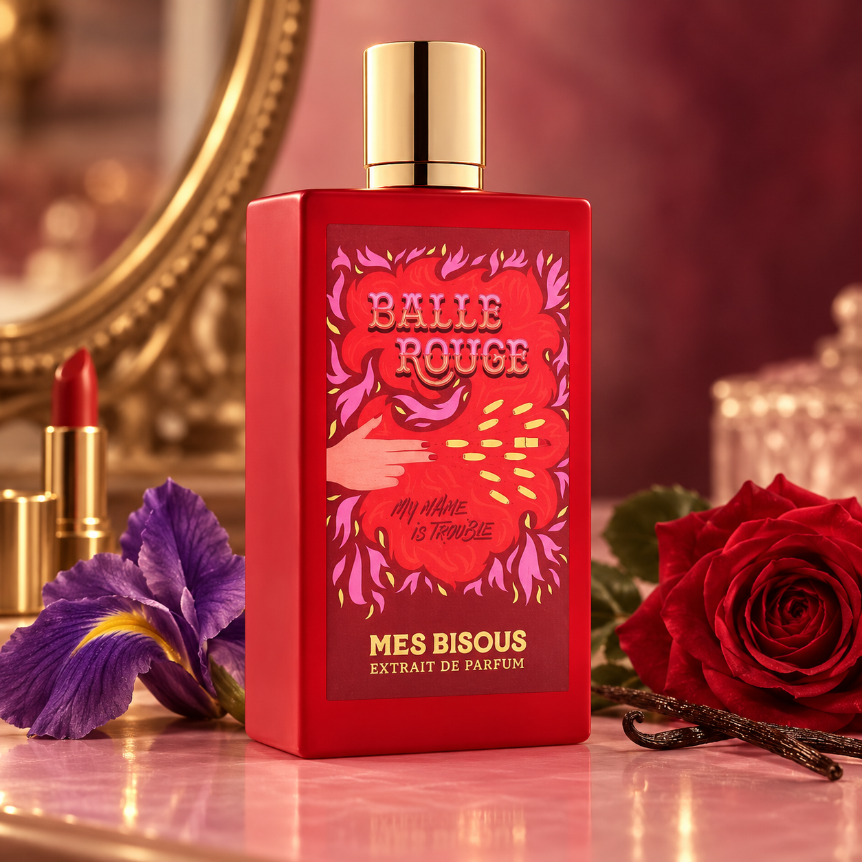 Mes Bisous Balle Rouge on a pink vanity beside iris, red rose, vanilla pods, and red lipstick, with a gold-framed mirror behind it.