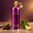 Aoud Greedy beside licorice root, a black licorice curl, patchouli leaves, and lemon on warm stone against a plum background.
