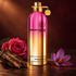 Montale Aoud Legend’s pink-and-gold bottle beside oud wood, a deep pink rose, and a saffron crocus on dark wood in warm light.