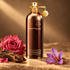 Montale Aoud Safran’s copper-brown bottle beside a pink rose, oud wood, and a purple saffron crocus on stone in warm golden light.