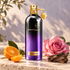 Montale Aoud Sense’s black-and-purple bottle beside mandarin, a pink rose, and oud wood on pale stone in soft sunlight.