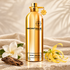 Montale Aoud Velvet’s gold bottle beside white tiare, yellow ylang-ylang, and oud wood on ivory stone with cream velvet behind it.