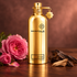 Montale Attar’s gold bottle on polished wood beside pink roses, dark oud, and pale sandalwood in warm light.