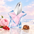 Mugler Angel Eau de Toilette’s pink and blue star bottle on pale stone beside a pink peony, redcurrants, and a praline chocolate in soft pastel light.
