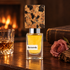 Nasomatto Baraonda on warm wood beside a whiskey tumbler, dusty rose, and aged wood, with a book and softly glowing fireplace behind it.