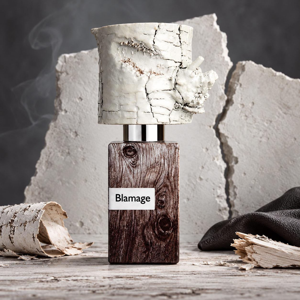 Nasomatto Blamage on weathered pale wood beside curled birch bark, splintered wood, and black leather, with fractured plaster and faint smoke behind it.