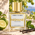Nishane Ambra Calabria bottle beside bergamot, glossy green leaves, and vanilla pods on pale stone in warm sunlight.