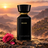 Omanluxury Dejan black bottle beside a pink rose and oud wood against misty terraced mountains at sunrise.