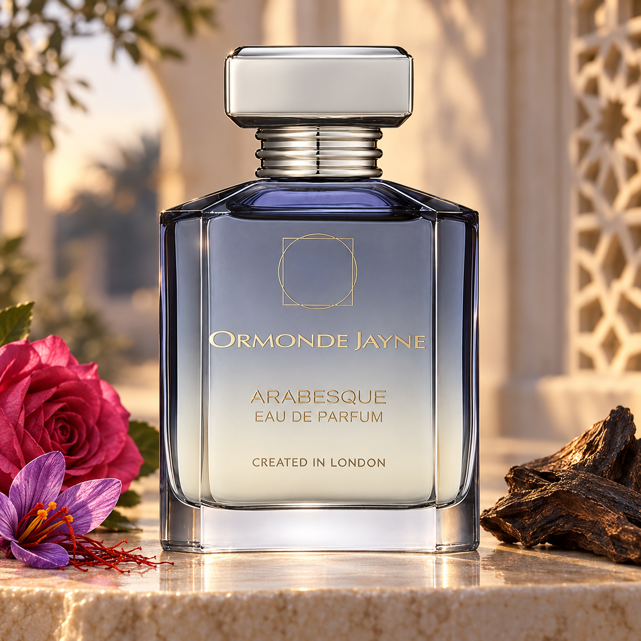 Ormonde Jayne Arabesque on ivory stone beside a pink rose, purple saffron crocus, and oud wood, with sunlit arches and a carved geometric screen behind it.