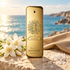 Paco Rabanne 1 Million Parfum gold bottle with white flowers, sea salt, and pale leather on sunlit stone overlooking the sea.