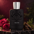 Parfums de Marly Akaster’s black bottle beside deep pink roses, agarwood, and cypress on dark stone under warm light.