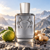 Parfums de Marly Castley beside bergamot, ginger, and black peppercorns on a rocky ledge overlooking sunlit mountains.