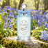 Penhaligon’s Bluebell bottle with a pale blue bow among dewy bluebells and moss in a sunlit woodland.