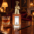 Penhaligon’s Clandestine Clara bottle with its gold bird cap beside rum, cinnamon and vanilla in a warmly lit salon.