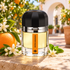 Ramon Monegal Entre Naranjos bottle beside a whole orange, orange blossoms and mint in a sunlit courtyard.
