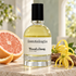Scentologia Wood.y².lang. beside grapefruit, yellow ylang-ylang flowers, and cedarwood on pale stone in soft daylight.