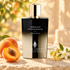 Simone Andreoli Apricot Innocence on sunlit cream stone beside ripe apricots, golden osmanthus, and white jasmine, with softly blurred foliage behind it.