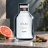 TUMI Atlas on cool gray stone beside pink grapefruit, cardamom pods, and sandalwood, against a softly lit blue-gray backdrop.