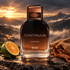 TUMI Continuum bottle on dark rock beside a green mandarin half, tobacco leaf, and suede, with misty mountains in golden light.