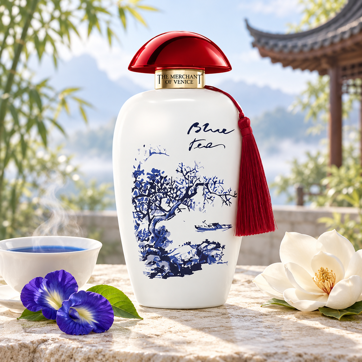 The Merchant of Venice Blue Tea beside steaming blue tea, butterfly pea blossoms, and magnolia on a misty garden terrace with a pavilion behind it.