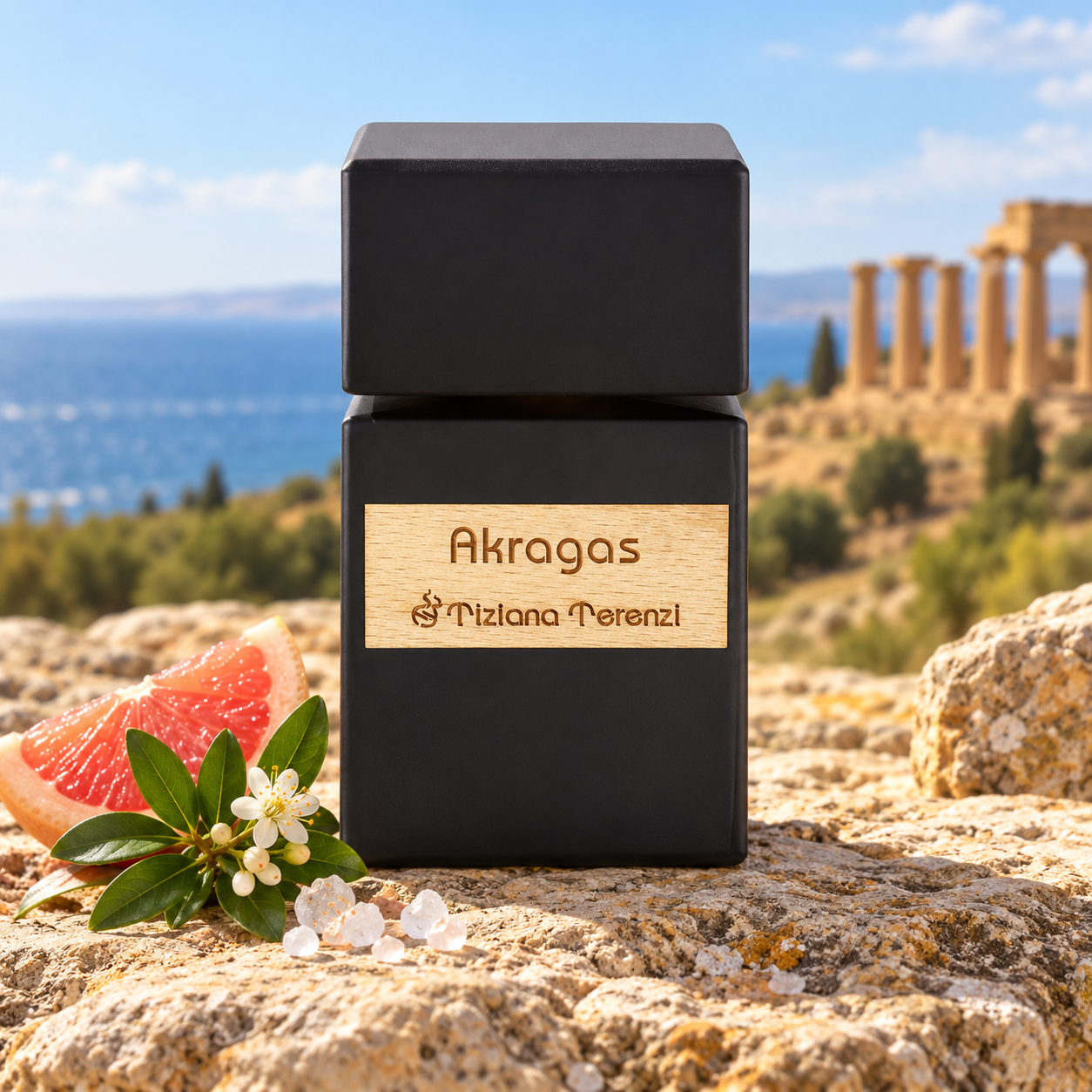 Tiziana Terenzi Akragas on sunlit limestone beside grapefruit, white myrtle blossoms, and salt crystals, with blue sea and ancient columns behind it.