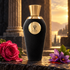 V Canto Boia on dark stone beside a pink rose, saffron crocuses, and patchouli leaves, framed by ancient columns and warm sunset light.