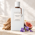 Van Cleef & Arpels Santal Blanc with sandalwood, a halved fig, and violet flowers on sunlit ivory stone.