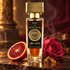 Wesker Eau de Mystique bottle beside a blood orange half, pink rose and incense resin on dark stone in warm golden light.