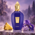 Xerjoff Accento purple bottle beside pineapple, iris, and hyacinth on pale stone against a softly lit, misty lavender background.