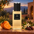 Yves Saint Laurent Atlas Garden on terracotta stone beside mandarin, orange blossoms, and dates, with a Moroccan-style garden and distant mountains at twilight.
