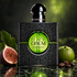 Yves Saint Laurent Black Opium Illicit Green on reflective dark stone beside a fig half, fig leaf, green mandarin, and coffee beans under green lighting.