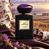 Giorgio Armani Cuir Amethyste black bottle with purple stone cap beside violet flowers, birch bark and plum leather against a misty grassland.