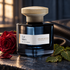 Atelier Materi Cuir Nilam dark blue bottle beside a red rose, patchouli leaves and black leather in warm atelier window light.