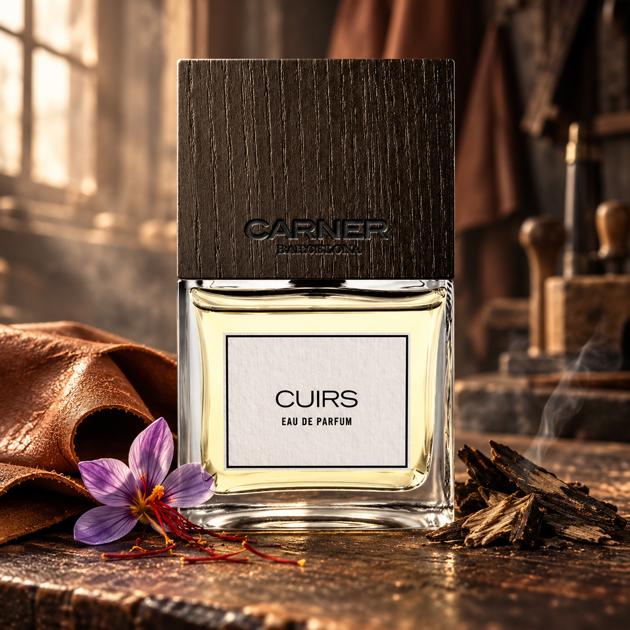 Carner Barcelona Cuirs bottle with dark wood cap beside cognac leather, a saffron crocus and guaiac wood on a warmly lit workbench.