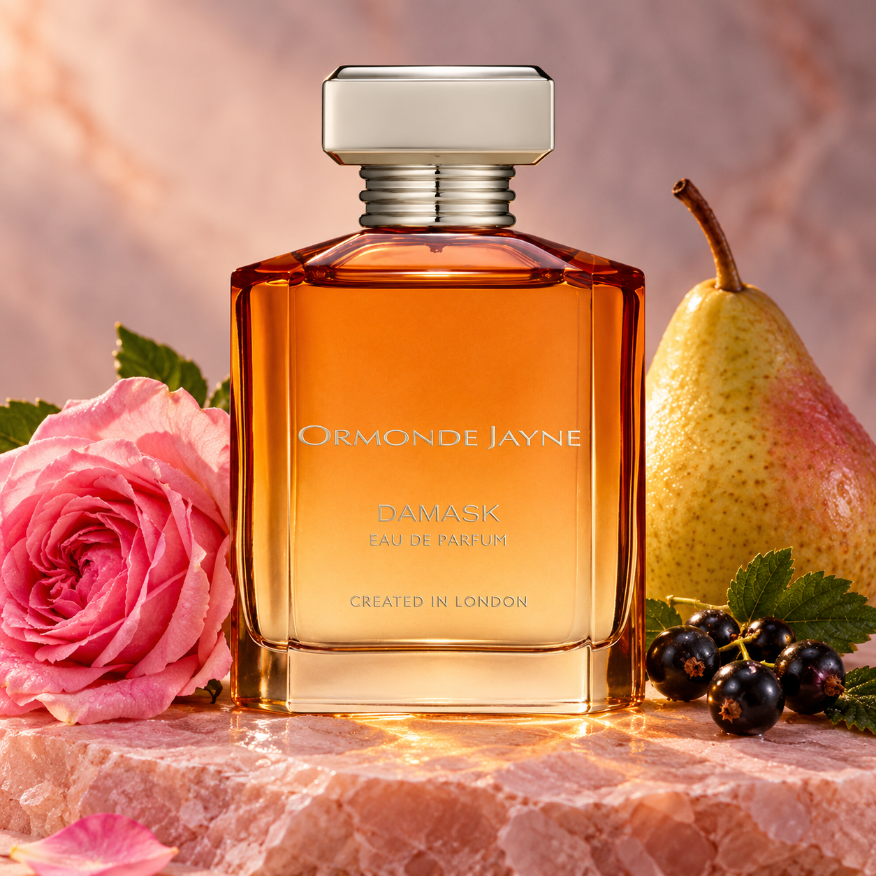 Ormonde Jayne Damask amber bottle beside a pink rose, whole pear and blackcurrants on pale pink stone in warm light.