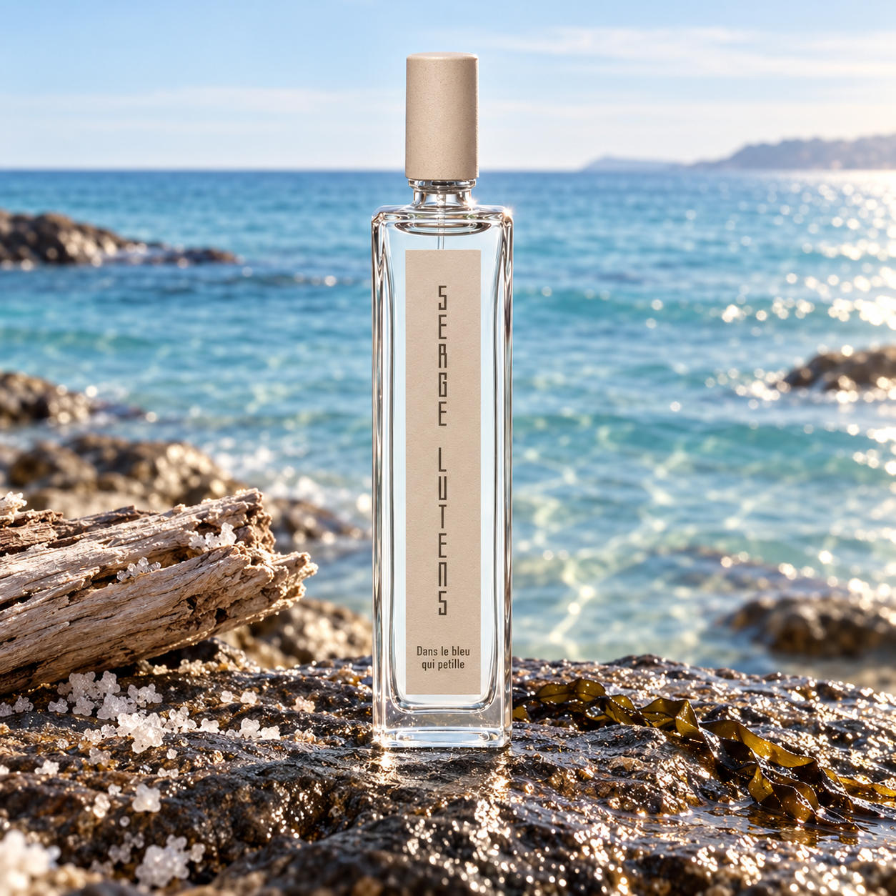 Serge Lutens Dans Le Bleu Qui Petille bottle on wet coastal rock beside driftwood, salt crystals and seaweed above a sparkling blue sea.