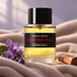 Frederic Malle Dans Tes Bras bottle beside violet flowers and sandalwood on soft taupe fabric in gentle window light.
