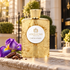 Atkinsons Gold Fair in Mayfair bottle beside purple iris and cacao on a sunlit ledge with London townhouses behind.