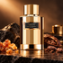 Carolina Herrera Gold Myrrh Absolute bottle with myrrh resin and cacao on black stone in bronze light.