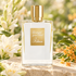 Kilian Good Girl Gone Bad bottle with white tuberose and orange osmanthus blossoms on sunlit garden stone.