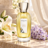 Goutal Grand Amour bottle beside white lily and pale purple hyacinth on ivory stone in soft daylight.