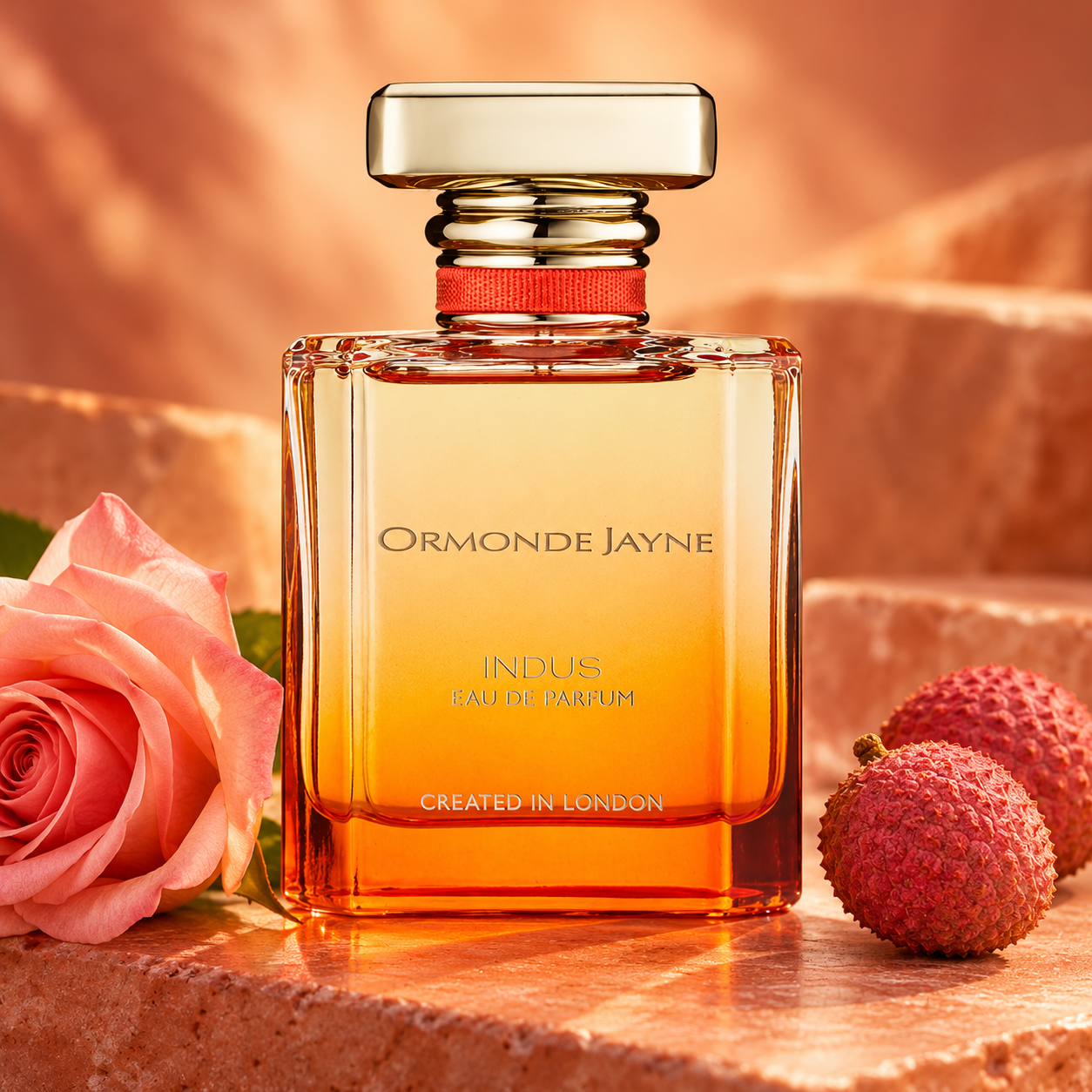 Ormonde Jayne Indus bottle with a pink rose and whole lychees on terracotta stone in warm orange light.